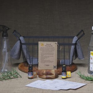 Black iron basket containing the Hearth & Larder Natural Cleaning Kit with vinegar, bicarbonate of soda, citric acid, spray bottles, reusable cloth, and cleaning booklet