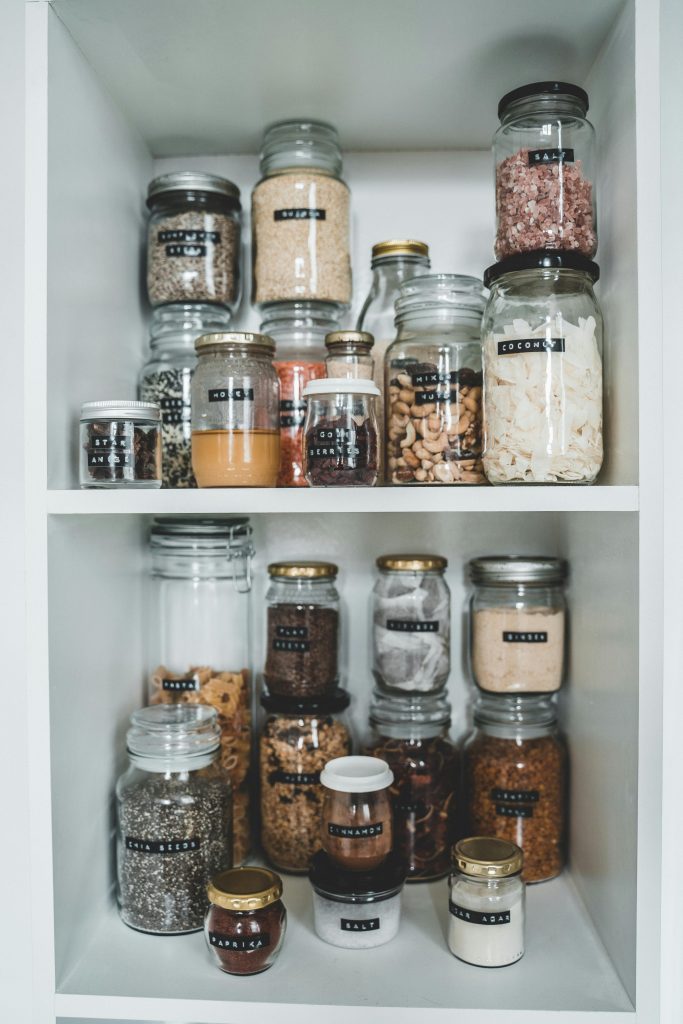 Clean pantry shelves displaying various food items stored in labeled glass jars.