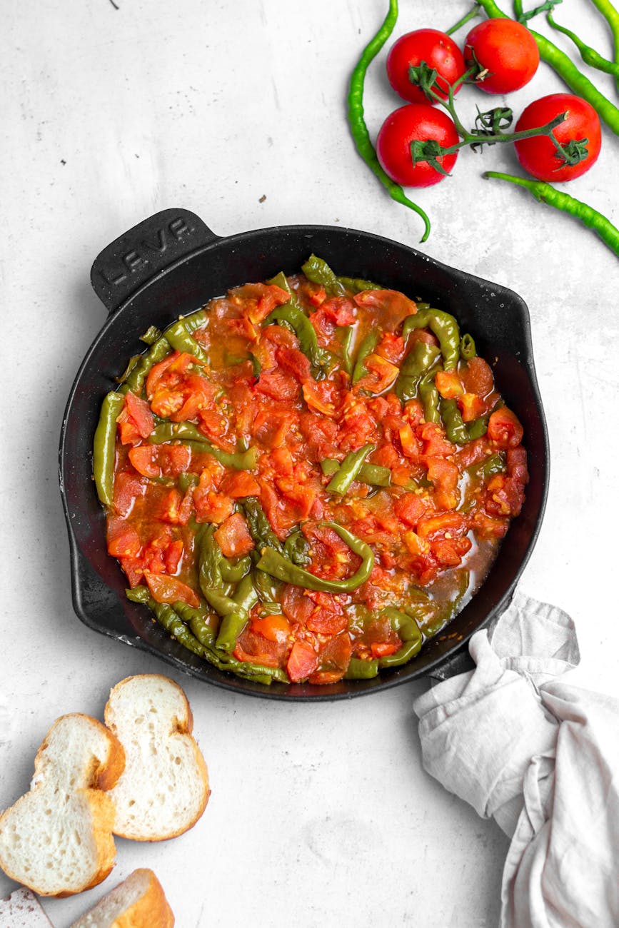 Top view of a vibrant vegetable stew with tomatoes and peppers in a cast iron skillet.